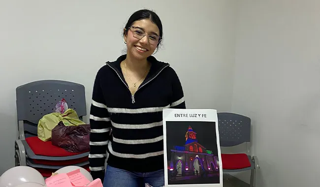 Estudiante junto a una mesa decorada con globos rosados y elementos simbólicos.