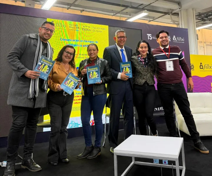 Docentes e investigadores de UNIMINUTO posan en el Auditorio del Pabellón Libro Técnico durante un panel académico sobre inteligencia artificial y comunicación, sosteniendo el libro "La comunicación en tiempos de IA: reflexiones académicas y desafíos comunicativos".