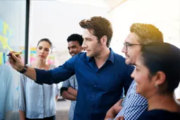 Grupo de personas colaborando y señalando información en una pantalla durante una reunión de trabajo.