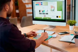 Persona utiliando una tableta digital frente a un computador mientras realiza un diseño