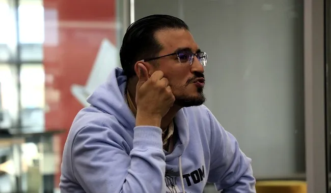 Hombre con gafas y sudadera clara apoyando la mano en la cara mientras habla expresivamente.