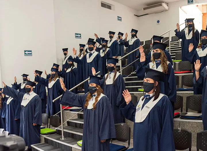 Estudiantes de píe usando toga azul con la mano derecha levantada haciendo juramento de grado 