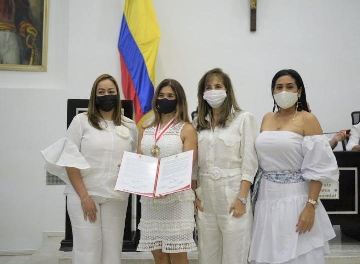Cuatro mujeres vestidas de blanco una tiene una medalla y pergamino de reconocimiento