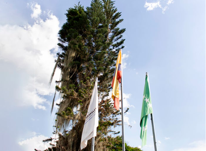 Banderas de uniminuto, colombia y risaralda, con paisaje de fondo 