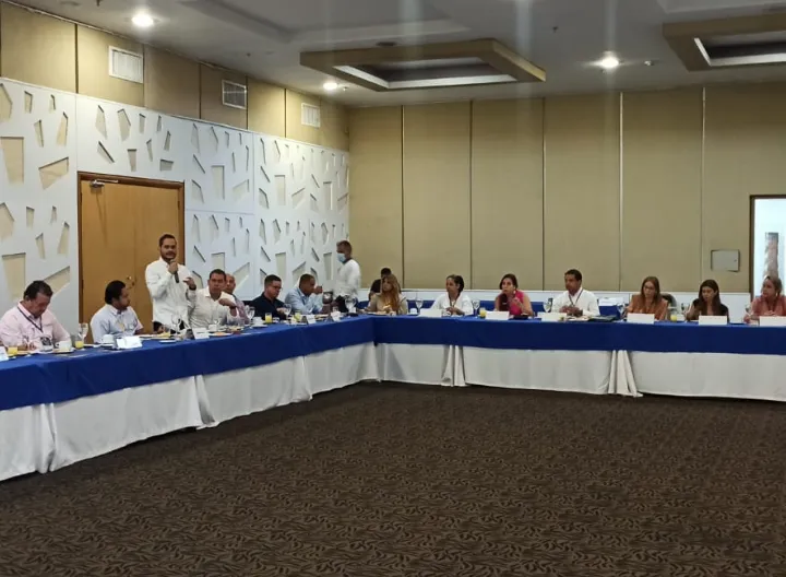 un hombre de pie hablando hacía varias personas sentadas en sillas en forma de U 