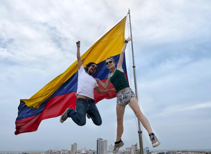 Jovenes saltando frente a una bandera de Colombia