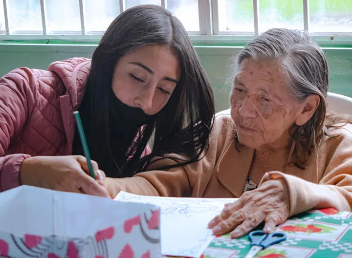 Estudiante UNIMINUTO enseñando a escribir a abuelita