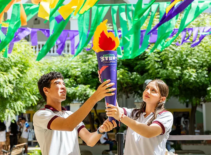 Dos estudiantes sostienen antorcha símbolo de inicio de las olimpiadas STEM 2025