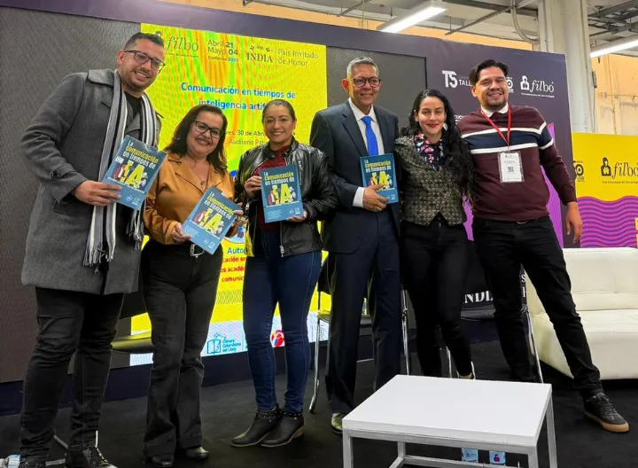 Docentes e investigadores de UNIMINUTO posan en el Auditorio del Pabellón Libro Técnico durante un panel académico sobre inteligencia artificial y comunicación, sosteniendo el libro "La comunicación en tiempos de IA: reflexiones académicas y desafíos comunicativos".