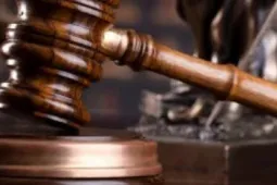 Balanza de la justicia junto a un mazo de juez sobre una mesa, con un reloj de arena y libros de derecho al fondo, representando el concepto de ley, justicia y paso del tiempo en los procesos legales.