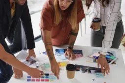 Grupo de tres personas trabajando en equipo alrededor de una mesa con documentos y materiales de trabajo.