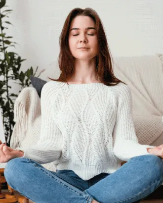 Mujer con los ojos cerrados, sentada con las piernas cruzadas y las manos sobre las rodillas