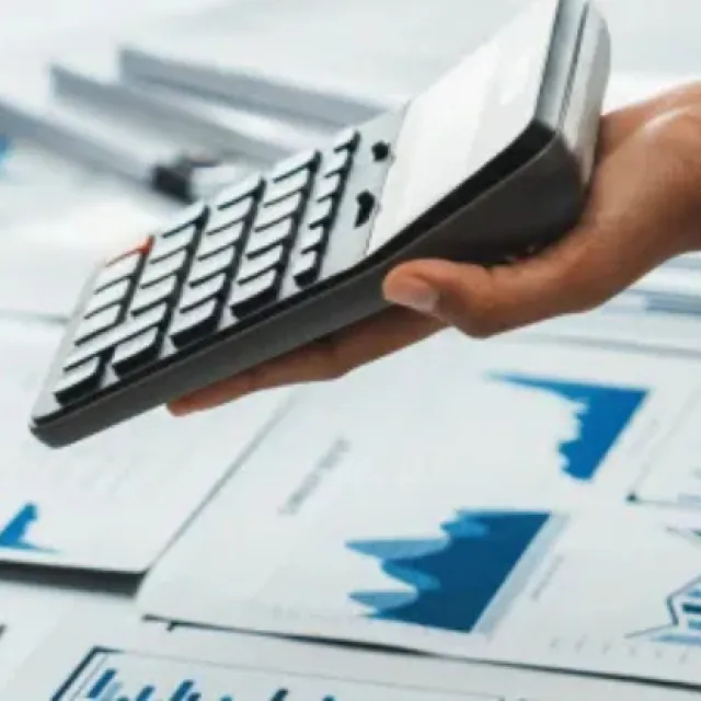 Manos de profesionales revisando gráficos financieros en una laptop y documentos impresos mientras utilizan una calculadora durante una reunión de análisis financiero.