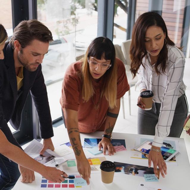 Grupo de tres personas trabajando en equipo alrededor de una mesa con documentos y materiales de trabajo.