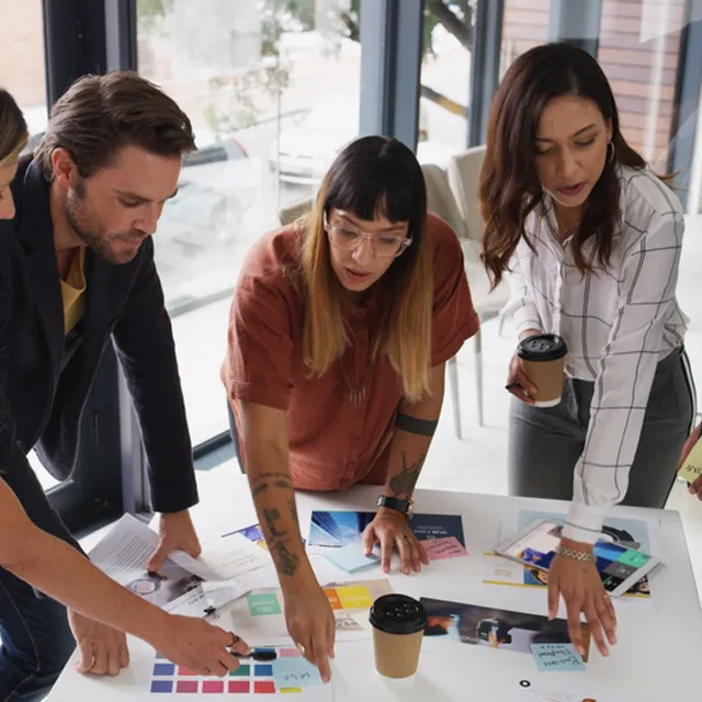 Grupo de tres personas trabajando en equipo alrededor de una mesa con documentos y materiales de trabajo.